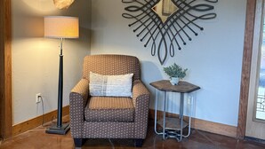Quarto com poltrona estampada, luminária, cabeça de veado fixada na parede e peça decorativa de metal.