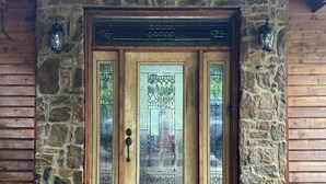 Entrada com parede de pedra e porta de madeira com painéis de vitral e puxador de metal.