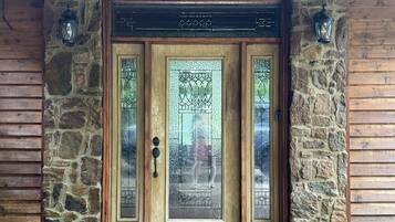 Une entrée en pierre, avec un mur de pierres, surmontée d’une porte en bois ornée de panneaux de vitraux et dotée d’une poignée de porte en métal.