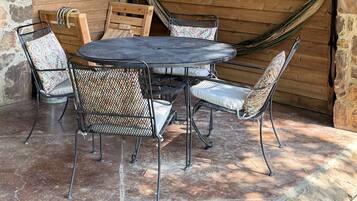Un espace extérieur abrité, avec une table ronde en métal et quatre chaises, un hamac et des murs en pierre.