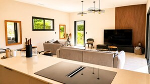 A modern living room with a large TV, a sofa, a dining area with a table, and a kitchen area with a countertop. - Casa Isula Di Santa Lucia (Sainte Lucie de Portio Vecchio)