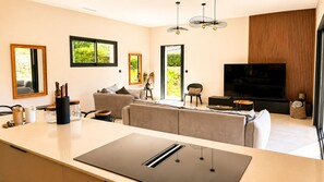 A modern living room with a large TV, a sofa, a dining area with a table, and a kitchen area with a countertop. - Casa Isula Di Santa Lucia (Sainte Lucie de Portio Vecchio)