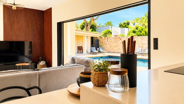 A modern kitchen with a large window, a pool, and a living area with a sofa and a TV. - Casa Isula Di Santa Lucia (Sainte Lucie de Portio Vecchio)