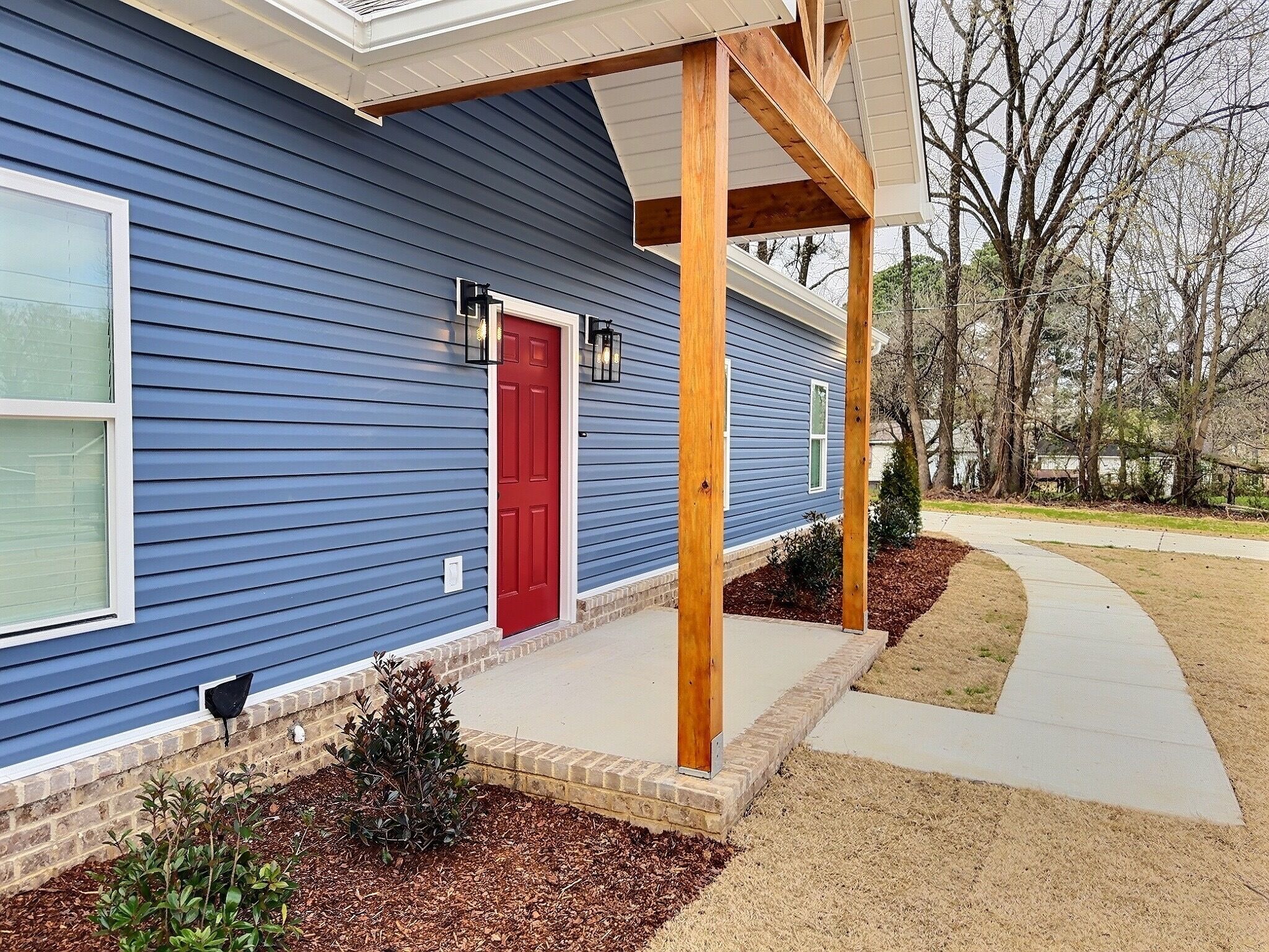 A residential house with a red door, a covered porch, and a landscaped front yard.