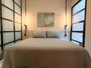 Ein Schlafzimmer mit einem Bett, zwei Kissen, einem Wandbild im abstrakten Stil und einem Fenster mit Blick.