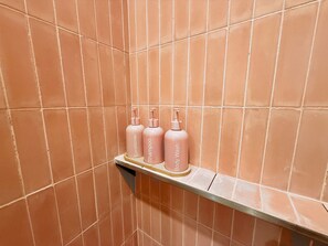 Ein Badezimmer mit einem Regal, auf dem drei Flaschen Duschgel und Conditioner stehen.
