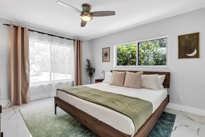 A bedroom with a bed, a ceiling fan, a window with a view, and a wall-mounted artwork. - NEW Beach Block Villa, Pool, Games (Pompano Beach)