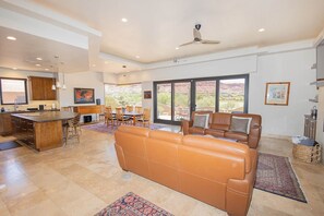 A spacious living area with a large brown leather sofa, a dining table with chairs, a kitchen with a bar area, and large windows offering a view of the outdoors. - Desert Retreat w/ Red Rock Views & Private Casita (St. George)
