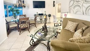 Un saló amb un sofà, una taula de café de vidre, una televisió, una pèndol i una zona de menjador amb cadires i una taula.