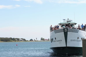 A ferry named Beaver Islander with passengers on deck, a lighthouse in the background, and calm water.