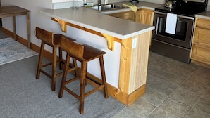 A kitchen with wooden cabinets, a granite countertop, a stainless steel sink, a coffee maker, a microwave, and an oven. - Flight Deck - 1-bedroom condo on Beaver Island, your perfect island retreat! (Beaver Island)