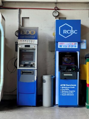 Zwei Geldautomaten, einer mit der Aufschrift BDO und der andere mit RCB, mit einem Mülleimer daneben.
