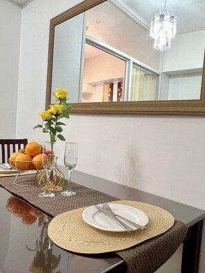 Ein Esstisch mit Untertischdecke, einem Teller mit Besteck, einer Vase mit gelben Blumen und einer Obstschale.