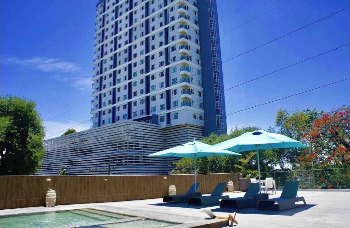 A high-rise building with a modern design, a swimming pool, and outdoor lounge chairs with umbrellas.