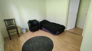 Una habitación pequeña y poco amueblada con piso de madera, una sola silla, un sofá negro, una cama y un tapete redondo.