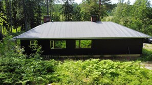 A house with a corrugated metal roof, surrounded by dense greenery and trees.