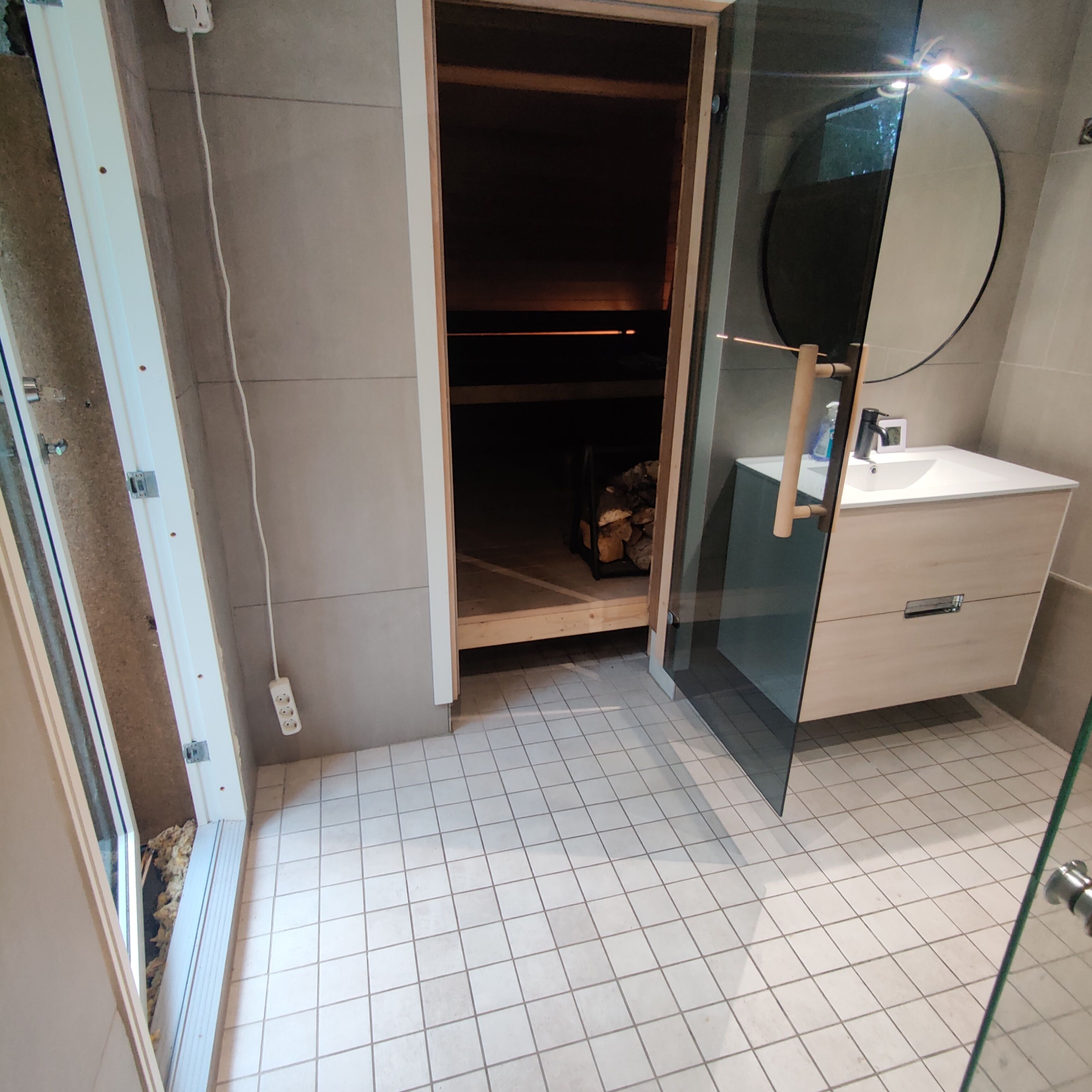 A bathroom with a glass shower enclosure, a white sink, and a wooden cabinet.