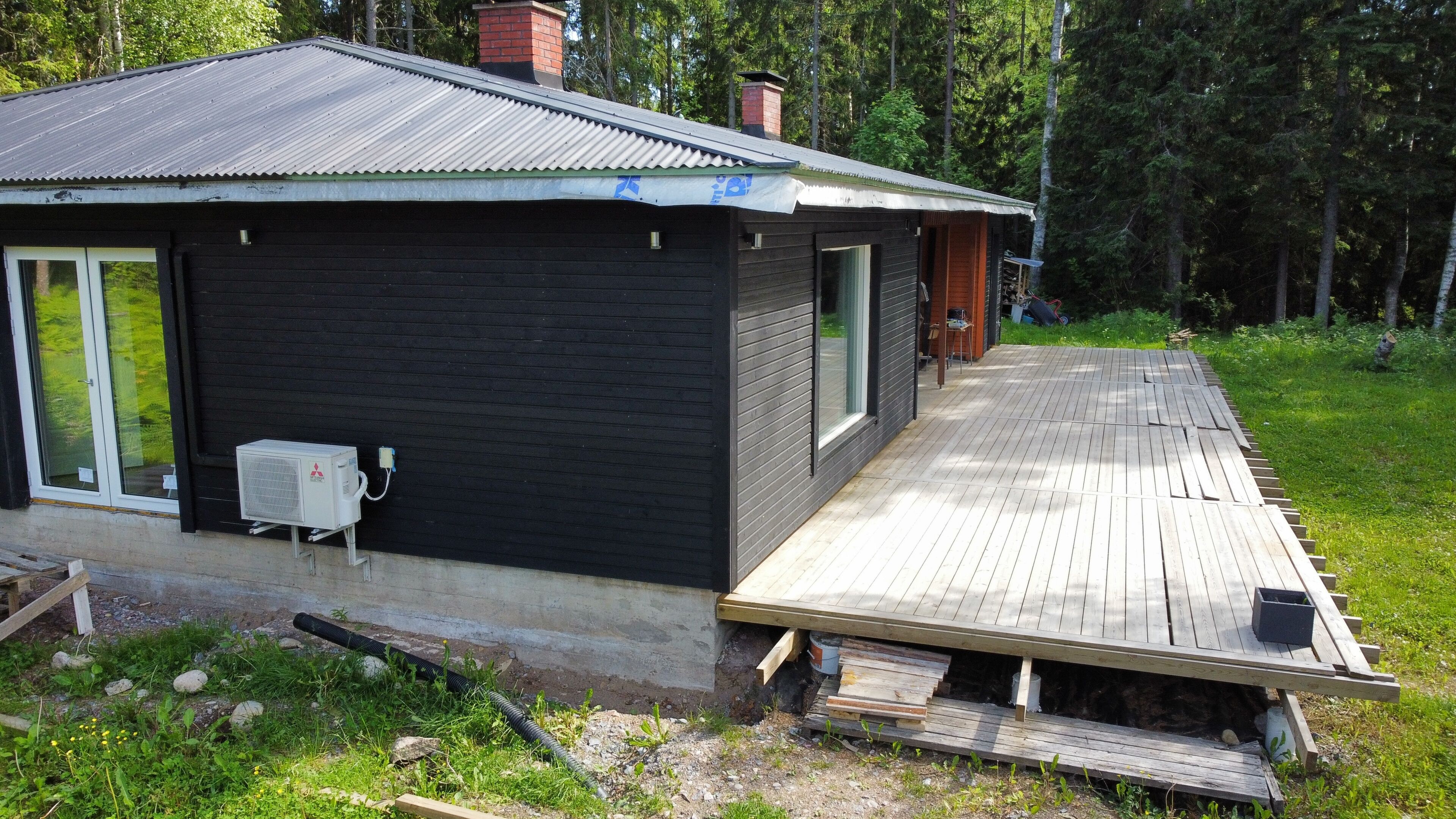 A black cabin with a wooden deck, a window, and an air conditioning unit.