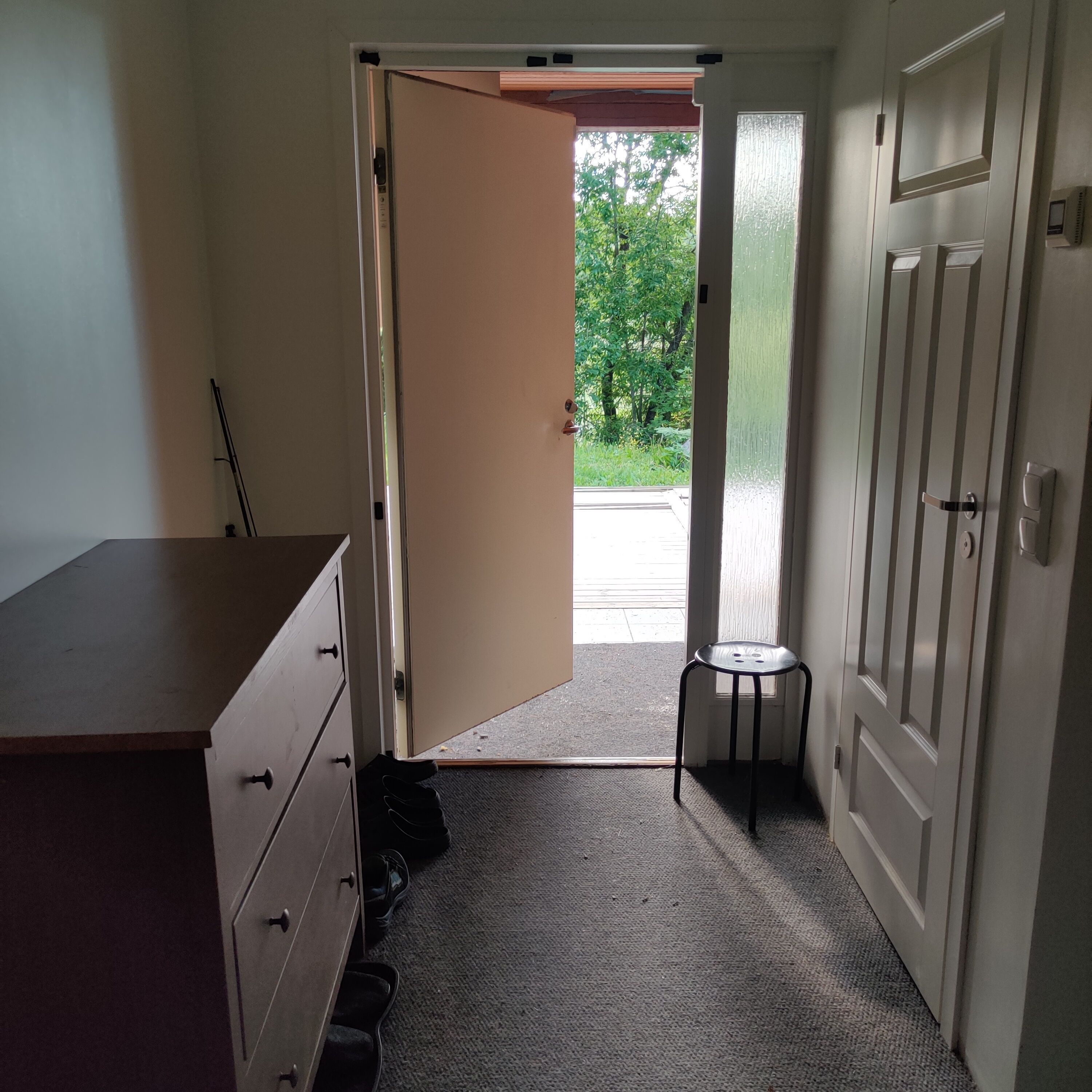 Un pasillo con una puerta que da al exterior, un taburete pequeño y un escritorio con cajones.
