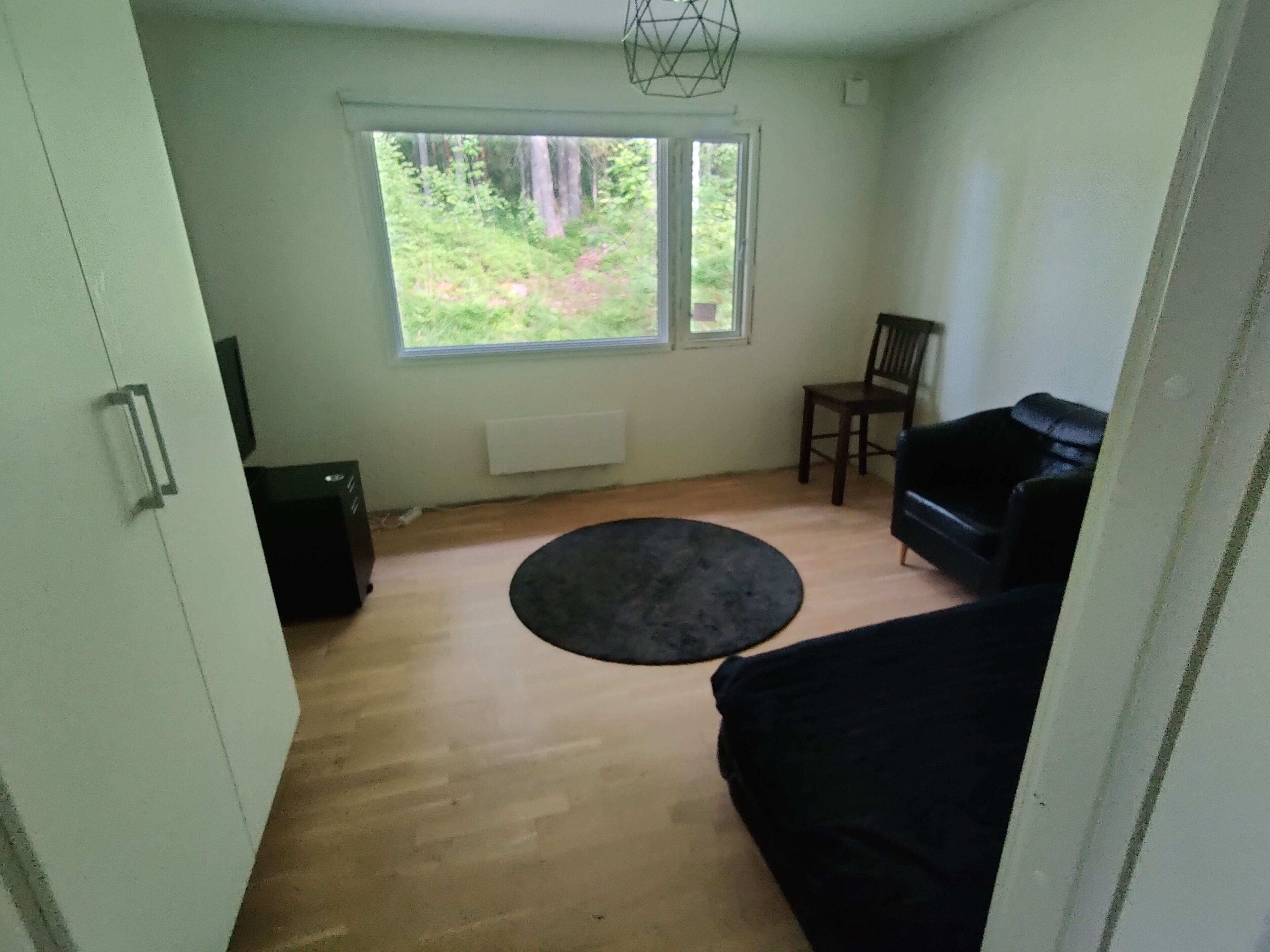 A room with a large window, a black sofa, a wooden floor, and a black circular rug.