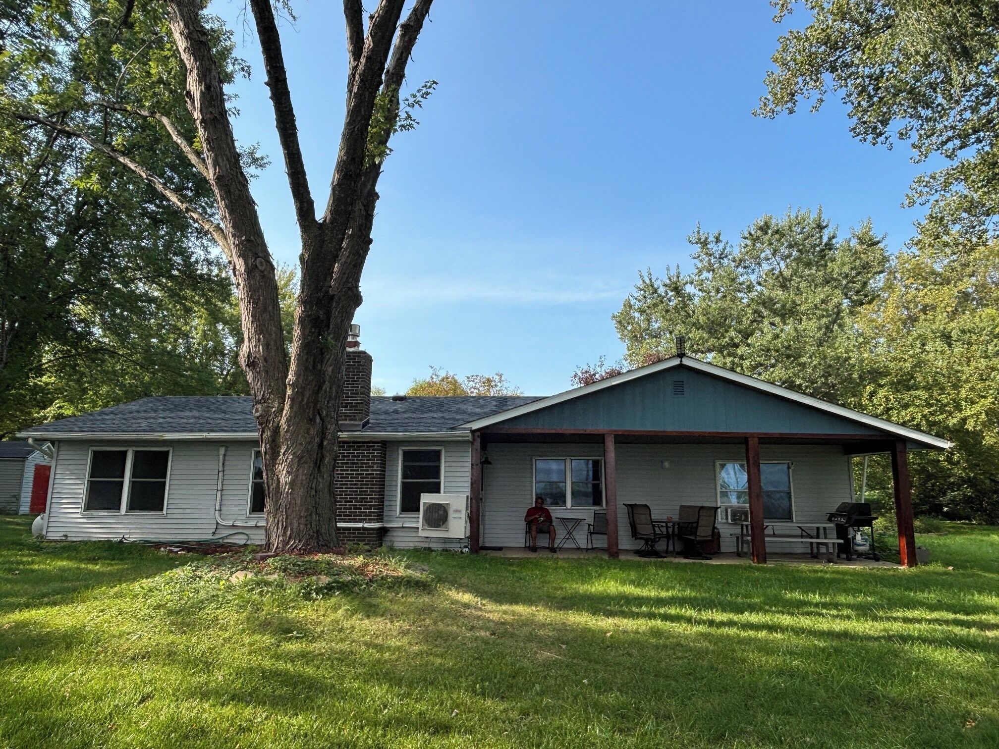 A single-story house with a covered porch, a large tree in front, and a well-maintained lawn.
