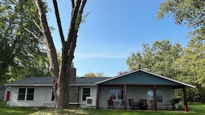 A single-story house with a covered porch, a large tree in front, and a well-maintained lawn.