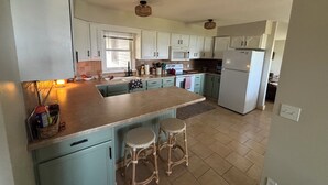 A kitchen with light blue cabinets, a central island with stools, a refrigerator, and a microwave.