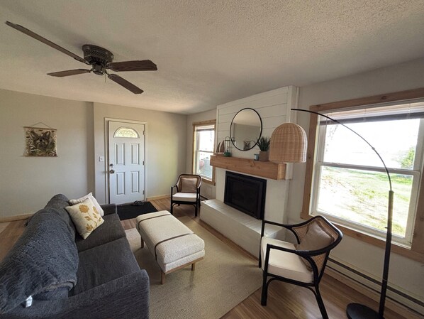 A living room with a fireplace, a ceiling fan, a sofa, and a chair.