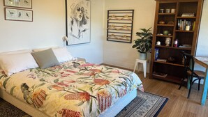 A bedroom with a bed, a bookshelf, a desk, and a wall with framed artwork.