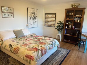 A bedroom with a bed, a bookshelf, a desk, and a wall with framed artwork.