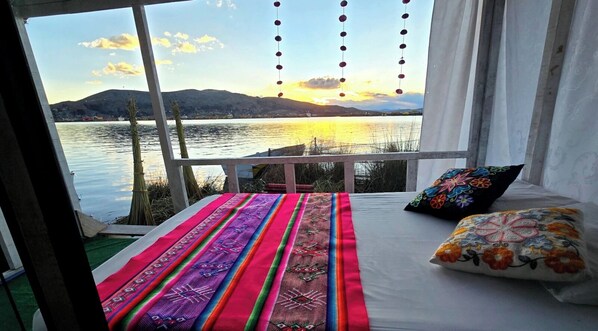 A bed with colorful pillows and a view of a lake at sunset.