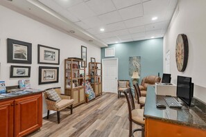 Ein Zimmer mit Schreibtisch, Computer, Stühlen, Bücherregalen und gerahmten Bildern an der Wand.