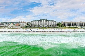 Ein Hotel direkt am Strand mit mehreren Etagen, ein Strand im Vordergrund und ein klarer Himmel.