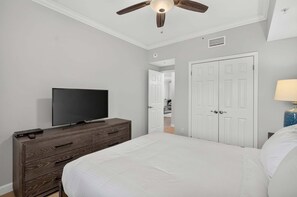 Ein Schlafzimmer mit einem Bett, einem Fernseher auf einer Kommode, einem Deckenventilator und einer weißen Tür.
