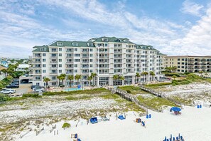 Ein großes Hotel mit mehreren Balkonen, einem Pool und einem Strandbereich mit Sonnenschirmen.