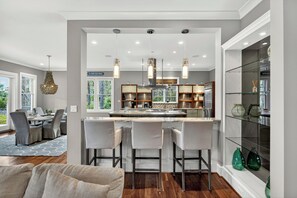 A modern kitchen with a central island, bar stools, pendant lighting, and a dining area with a view. - AMAZING Marsh-view Kiawah Island home with 5 BDs, private pool! (Kiawah Island)