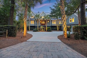 A two-story house with a central entrance, surrounded by a landscaped garden with palm trees and a paved driveway. - AMAZING Marsh-view Kiawah Island home with 5 BDs, private pool! (Kiawah Island)