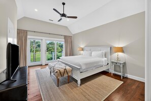 A bedroom with a bed, a TV, a ceiling fan, a nightstand, and a view of the outdoors. - AMAZING Marsh-view Kiawah Island home with 5 BDs, private pool! (Kiawah Island)