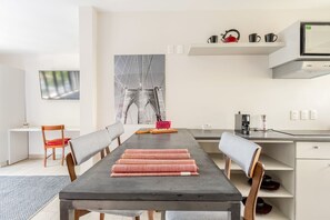 Ein moderner Essbereich mit einem langen Tisch, Stühlen, einer Küchenzeile mit Mikrowelle und einem großen gerahmten Bild an der Wand.