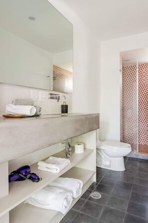 A modern bathroom with a large mirror, a toilet, a shower with patterned tiles, and neatly folded towels on the counter. - Loft Cama King en el Corazón de Coyoacán (Ciudad de México)