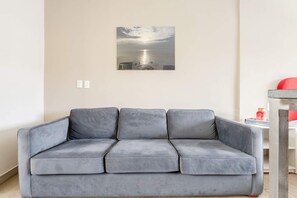A grey sofa in a room with a wall-mounted picture of a sunset over water. - Loft Cama King en el Corazón de Coyoacán (Ciudad de México)