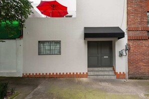 Ein Gebäude mit weißer Fassade, einer grauen Tür, einem kleinen Fenster und einem roten Regenschirm.