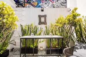 Eine Terrasse mit Tisch, zwei Schädeldekorationen, Topfpflanzen, einer Wand mit Wandgemälde und einem spiegelnden Wandbild mit Metallrahmen.