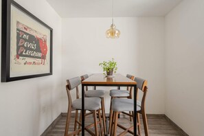 Ein Essbereich mit einem Holztisch, sechs grauen Stühlen, einer hängenden Pendelleuchte und einem gerahmten Bild an der Wand.