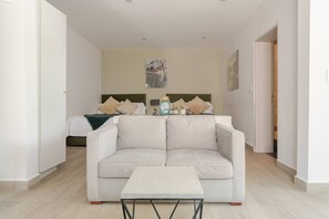 Ein modernes Hotelzimmer mit einer Couch, einem kleinen Tisch, einem Bett mit Kissen und einem an der Wand hängenden Kunstwerk.