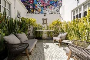 A courtyard with a colorful mural, wicker furniture, and potted plants. - Apartamento de 1 dormitorio (Diego) (Ciudad de México)