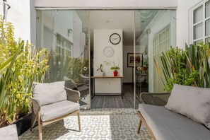 A sunlit patio with wicker furniture, a glass door leading to an interior space, and potted plants. - Apartamento de 1 dormitorio (Diego) (Ciudad de México)