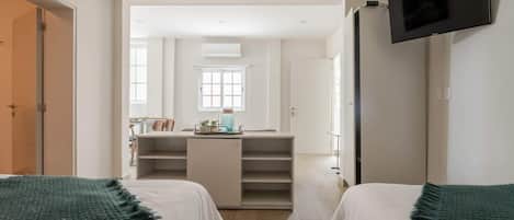 Ein Schlafzimmer mit zwei Betten, einem an der Wand befestigten Fernseher, einem Schreibtisch mit Stuhl und einem Fenster.