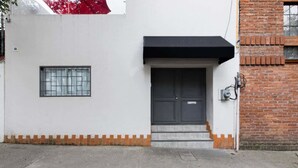 Un edificio con facciata bianca, una porta nera, una piccola finestra e un muro in mattoni.