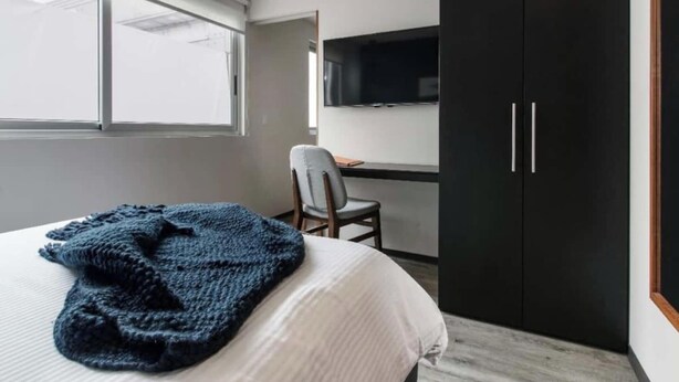 Una camera da letto con un letto, una scrivania con una sedia, una TV a parete e un armadio.
